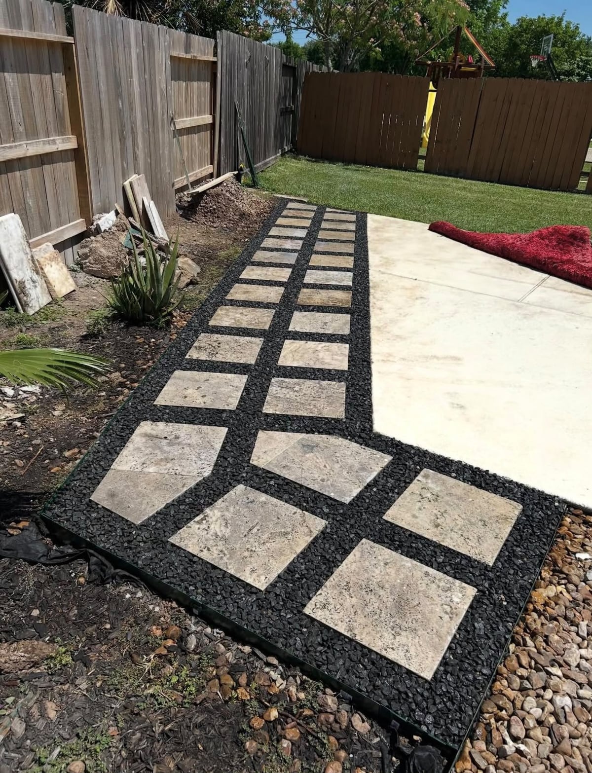 Completed double-row stone walkway set in dark gravel beside a backyard patio